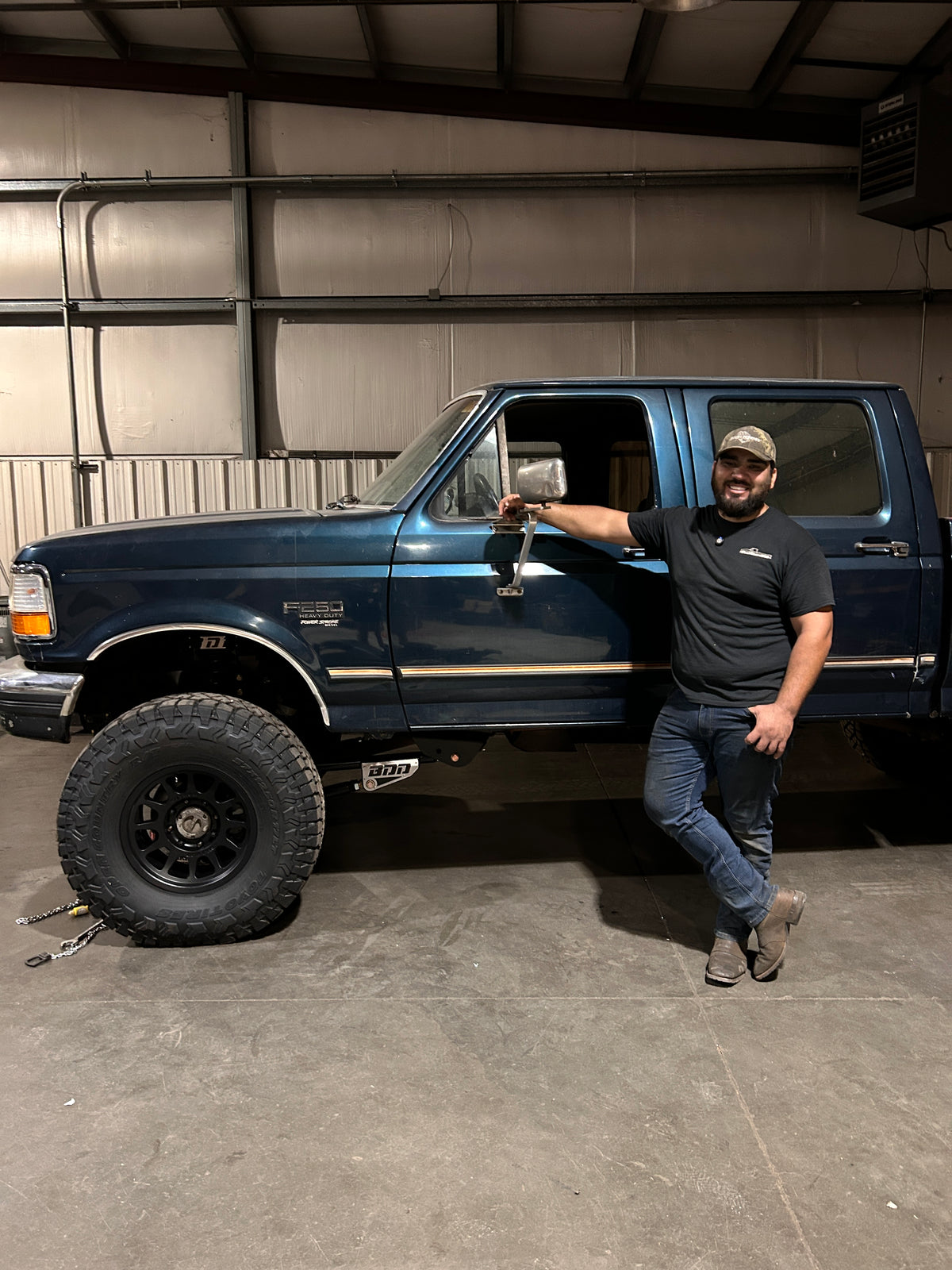 Joel Dominguez standing next to recently 2005+ axle swapped blue OBS truck with 4" of lifted inside the BDD garage shop.