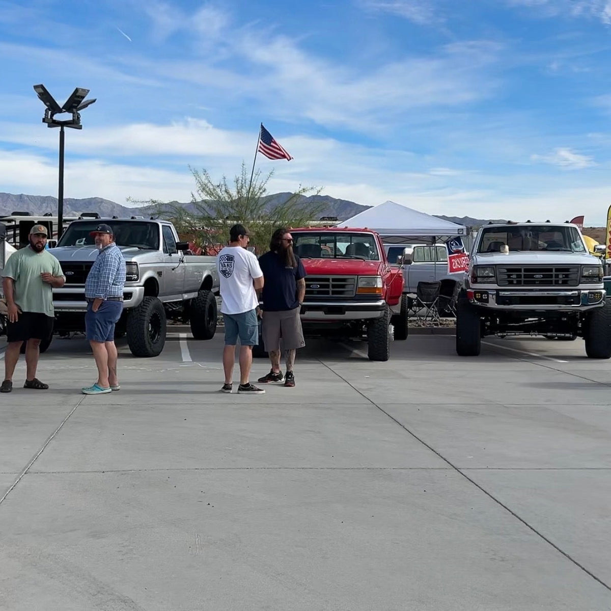 Joel Dominguez standing with friends in a large concrete lot at the Southwest Ford Nationals Truck Show in Lake Havasu City, AZ. Three  OBS Ford trucks being displayed in BDD booth